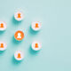 Cylinder objects with human symbols on blue background. One of the objects is orange colored. Horizontal composition with copy space.