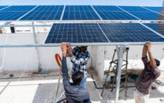 Getty, Indian workers installing solar panels on roof of house.