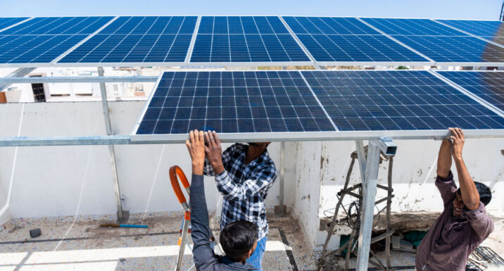 Can blended finance reach scale for emerging market climate action? Getty, Indian workers installing solar panels on roof of house.